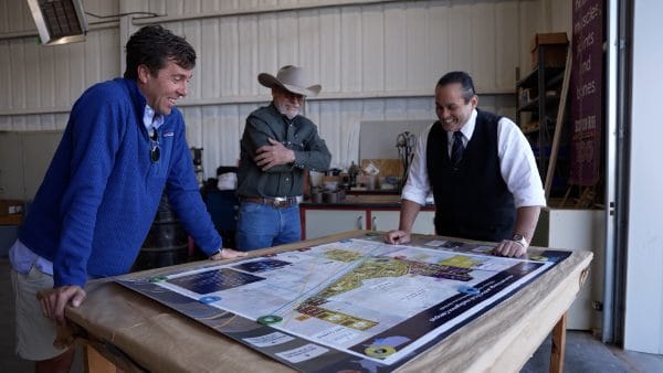 Three men standing around a table with a large map on it.