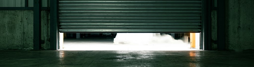 A warehouse door partially raised with light spilling out