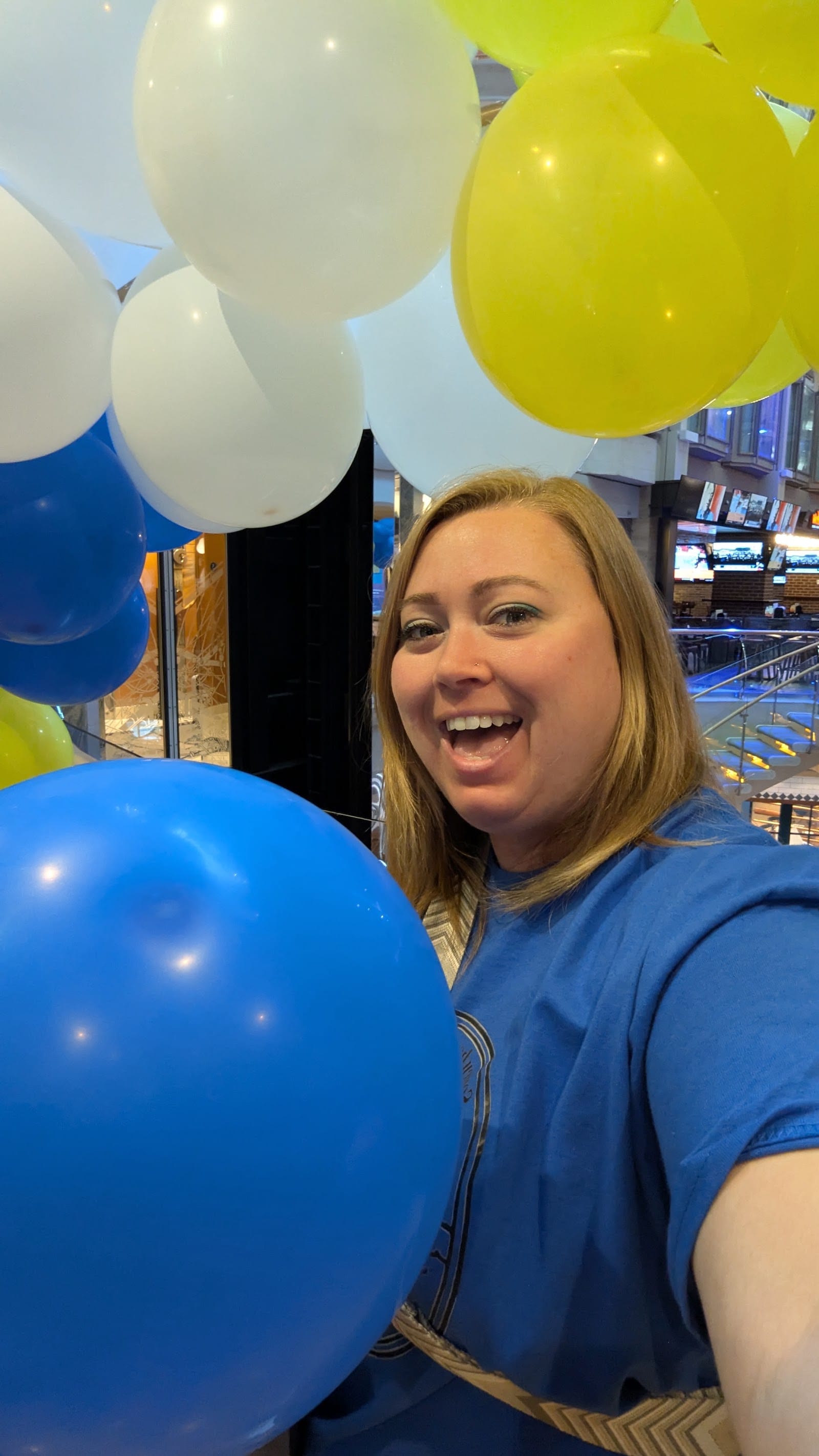 A smiling Somewhere Beyond Vacations advisor in a blue SBV shirt laughing among balloons at a team event