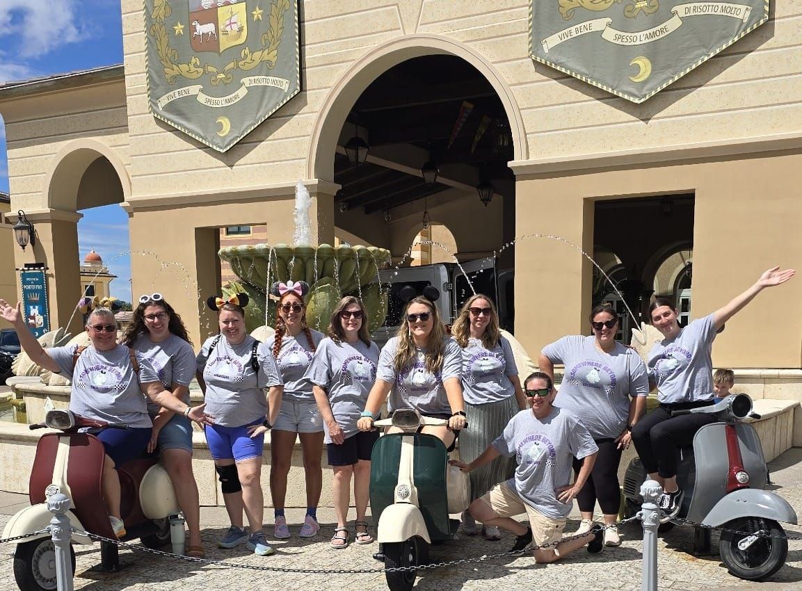 A group of Somewhere Beyond Vacations travel advisors in matching gray SBV shirts posing together with Vespas in front of the Provincia di Portofino banners