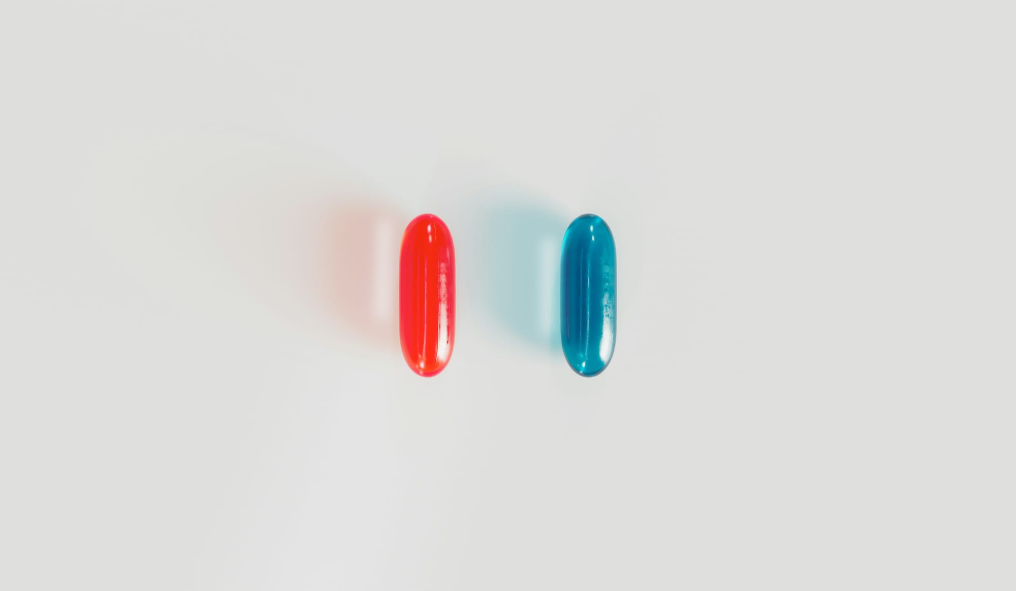 A red pill and a blue pill side by side on a white table.
