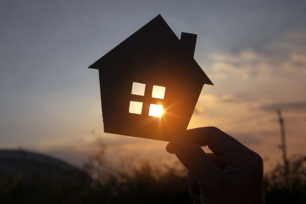 Hands holding paper house on sunset sky, family home, homeless housing, and home protection insurance concept, international
