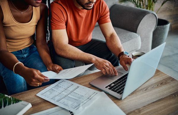 Cropped shot of an unrecognisable couple sitting in the living room and using a laptop to calculate their finances
