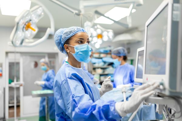 Anesthetist Working In Operating Theatre Wearing Protecive Gear checking monitors while sedating patient before surgical proc