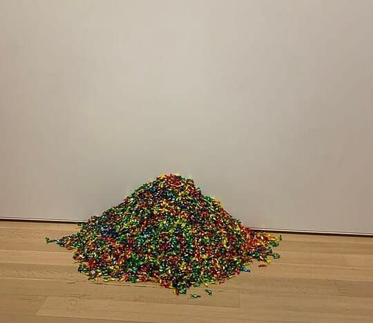 A pile of multi colored candies on a wooden floor with a gray wall behind
