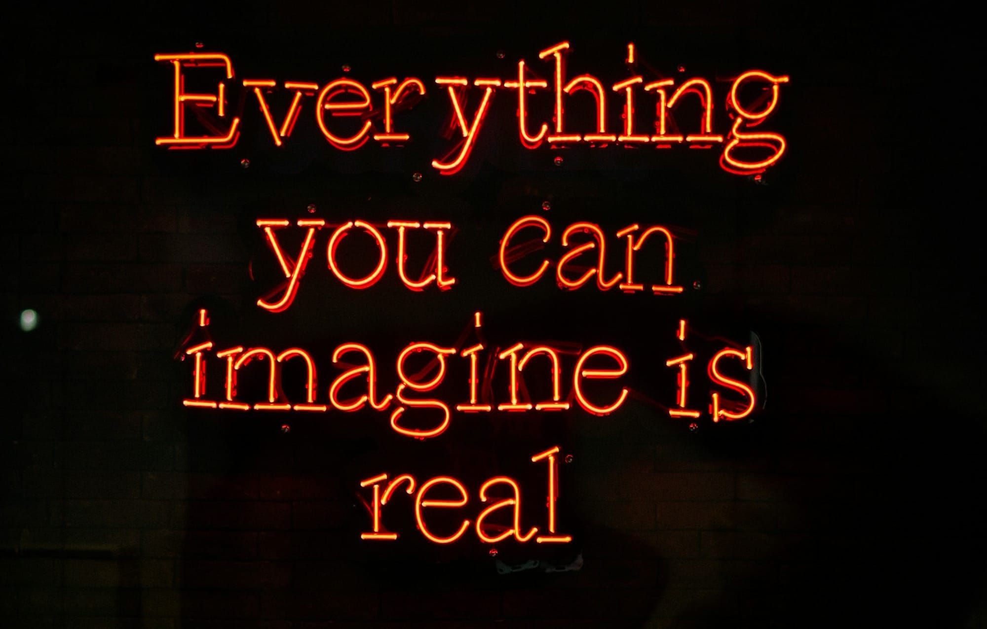 Orange neon letters spell "Everything you can imagine is real" against a black background
