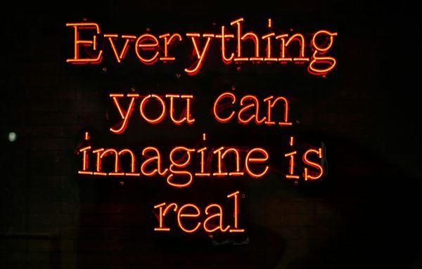 Orange neon letters spell "Everything you can imagine is real" against a black background