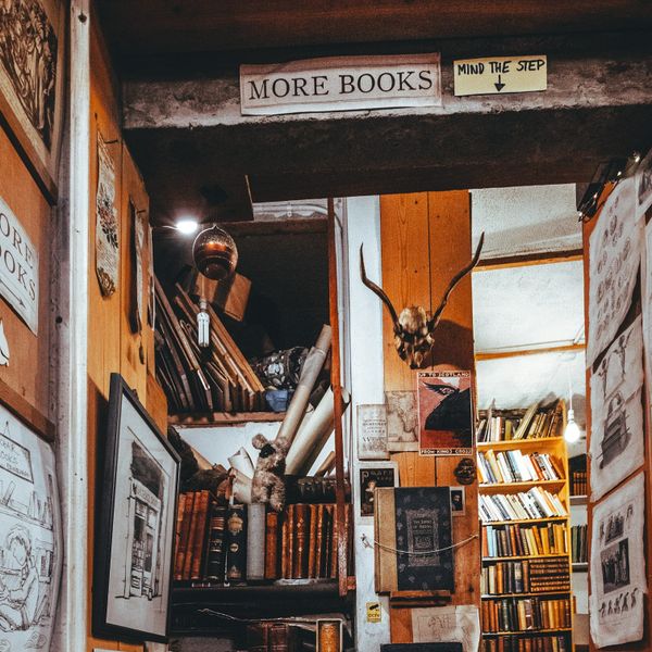 crowded stairwell with sign reading more books. walls are covered with books, shelves, and ephemera