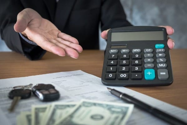 Auto insurance paperwork, calculator, and cash on a desk, representing the cost of car insurance and financial decision-making