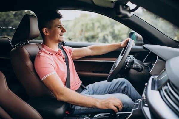 Man smiling while driving a car with brown leather interior, seatbelt fastened