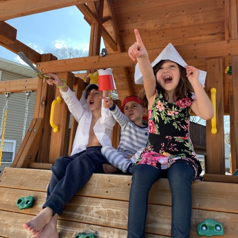 3 kids wearing paper pirate hats pretending to be on a ship
