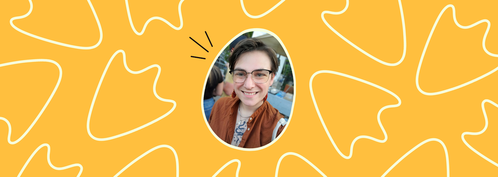 Headshot of a person smiling. They are wearing black wire-rimmed glasses and a brown shirt