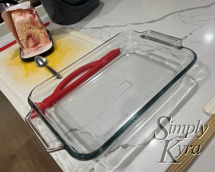 An empty 9 by 13 glass casserole dish with half a softened cheesecake behind it. 