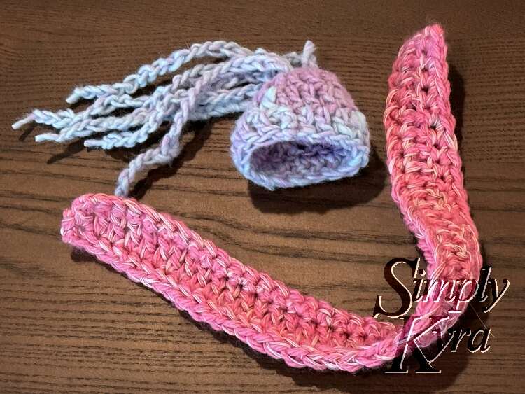Flat lay with the hat on its side with the hair to the left. The scarf is bent in the center to frame the hat below and to the right.