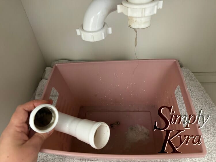 Image shows the curved pipe sideways showing the gunk inside with a hair hanging from the main pipe and gunk in the pink plastic bin.