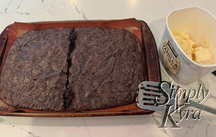 Now baked and dry the brownie on the silpat lined cookie sheet is cut in half, next to a metal flipper, and has ice cream beside it.