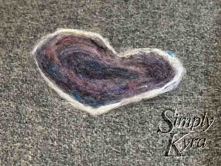 Image shows a closeup of the just finished heart with a. white border and swirls of blue and purple. 