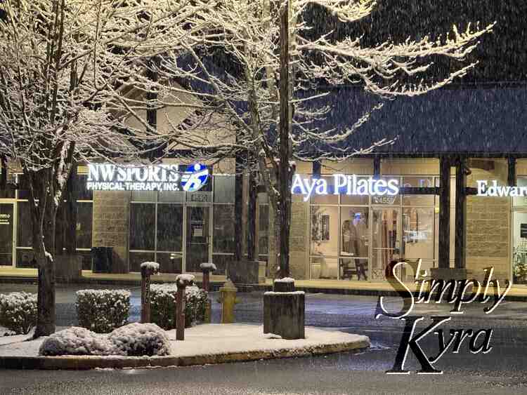 View of Aya and surrounding stores with snow falling and staying. Taken in the dark.