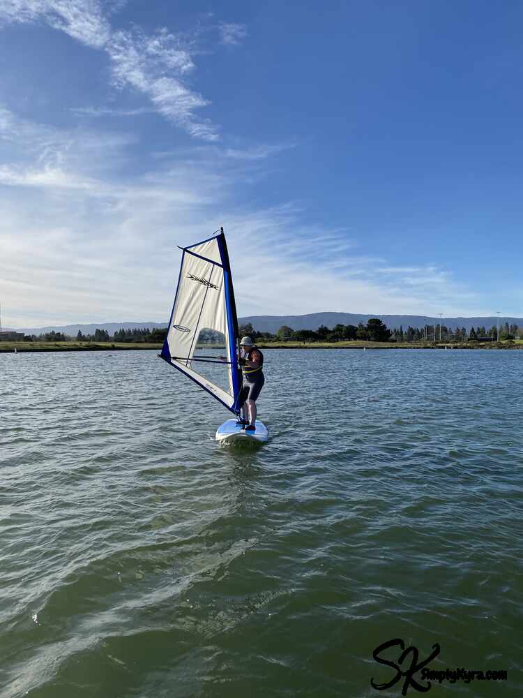 Image of me on a blue surfboard wearing a borrowed wetsuit and sunhat.