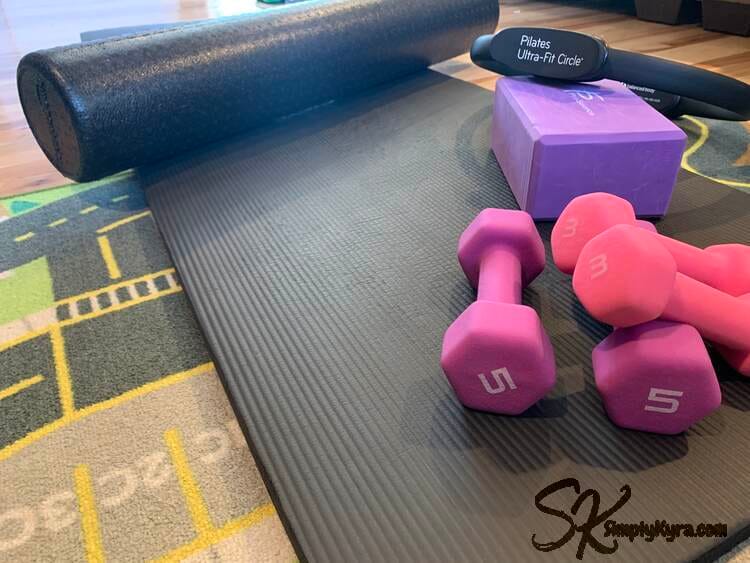 The tools laid out for a photo on the car mat... pictured if thick pilates mat, foam roller, foam yoga block, magic ring, and two sets of weights: 3 and 5 lbs.