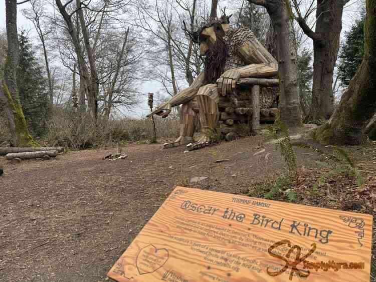 The king points to the bench logs from behind the sign.