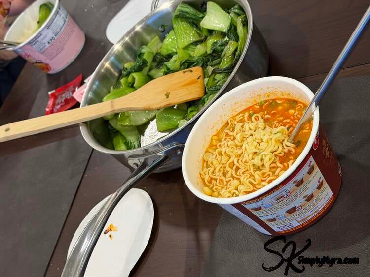Table with two different bowls of ramen and a pan of bok choy between.