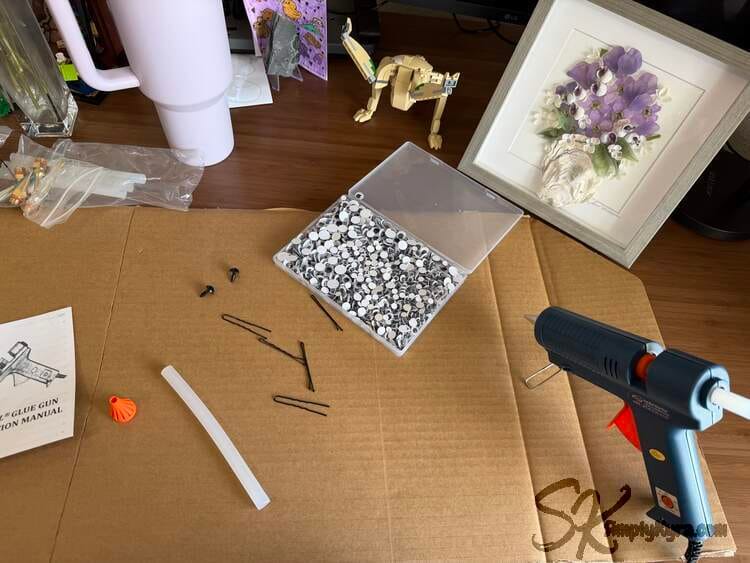 Gun plugged in and heating up, bobby pins (two types) laid out, old crochet eyes still out (was going to use), and an open container of googly eyes.