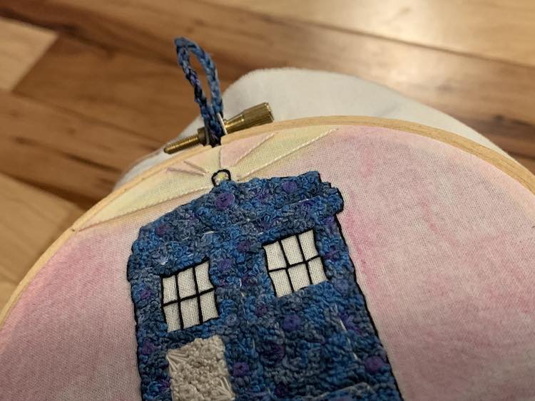 Closeup of the top of my embroidery hoop with the fabric centered and pulled taunt and the matching loop of fabric at the top to hang it up with.