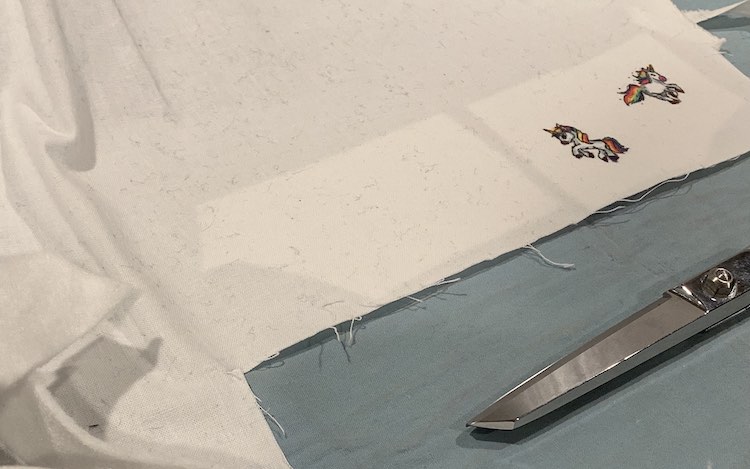 The fabric is laid out on a blue ironing pad. You can tell where the interfacing is attached to the back as the fabric is whiter there. There are two patches of white and both the unicorns are on the right-most patch. 