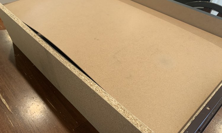 Zoey’s dresser drawer is upside down on the kitchen table. From this vantage point you can see the center of the drawer base sticking up (slanted like a hill) with an empty space under it at it’s peak.