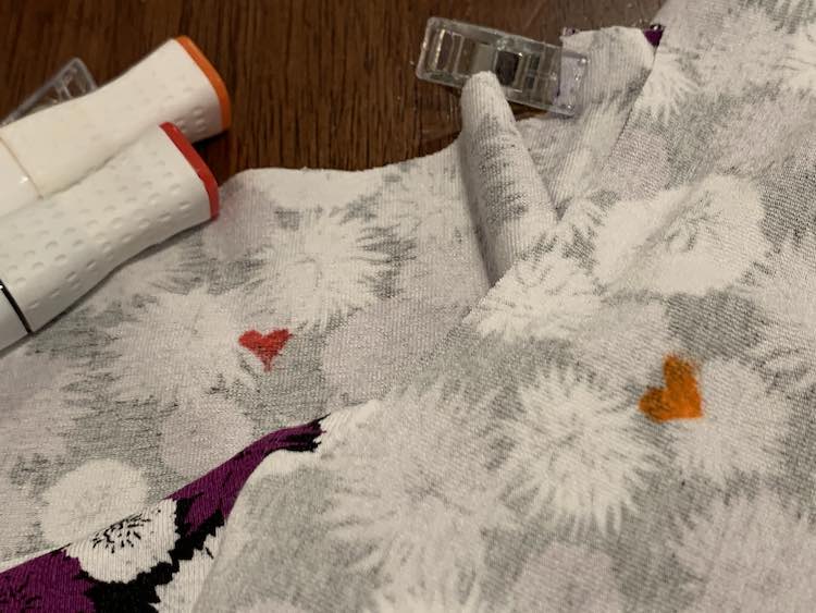 Closeup of the back of both bodices (overlapping) overlaid with the two fabric markers I used. You can see an orange heart on the upper bodice piece and a red heart below.
