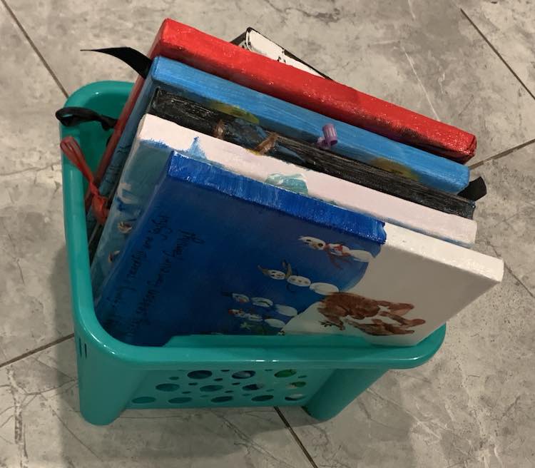 Dollar Tree plastic teal basket with all the canvases ordered by holidays within it. It's missing the Thanksgiving sign since that's currently beside the front door.