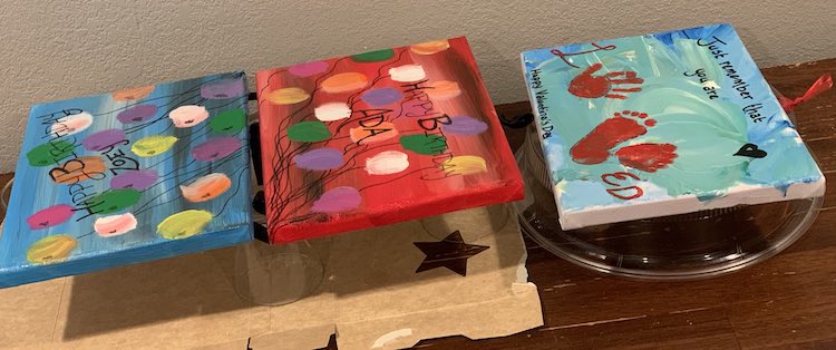 The two Happy Birthday signs are propped up on glass cups on an opened cardboard box, like before, while the Valentine's Day loved sign is on a microwave dish cover to the right.