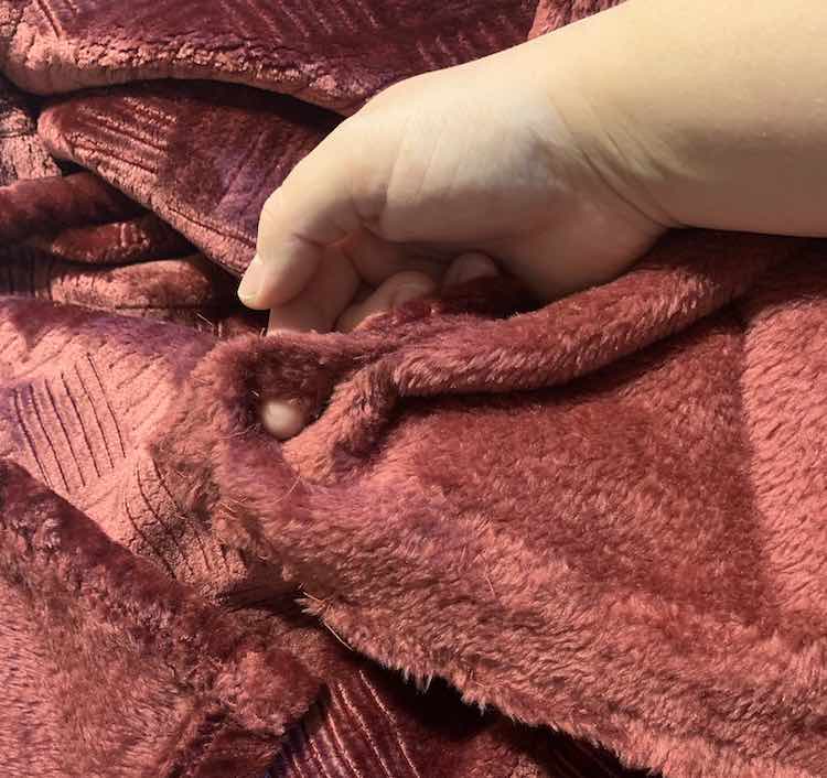 Reddish throw with a corner of it being held in my hands and a finger going through the hole in it. 