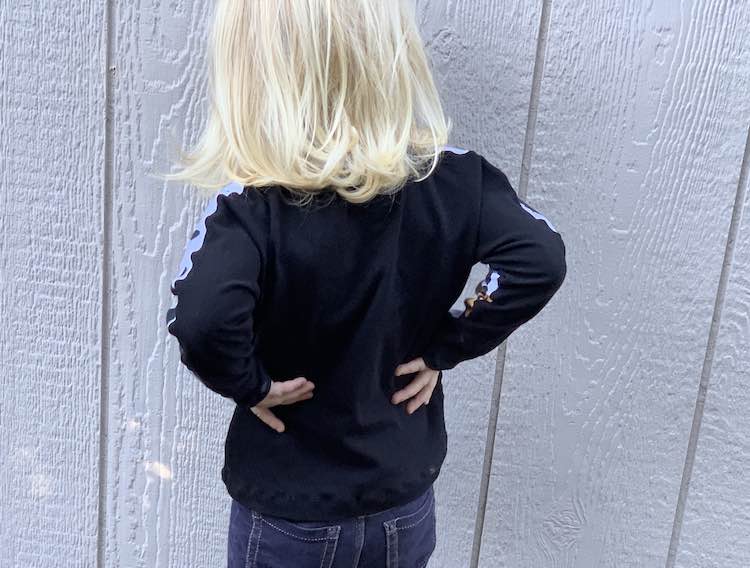 Back view of the pumpkin shirt. Zoey's hands are on her hip and you mostly see the black fabric.
