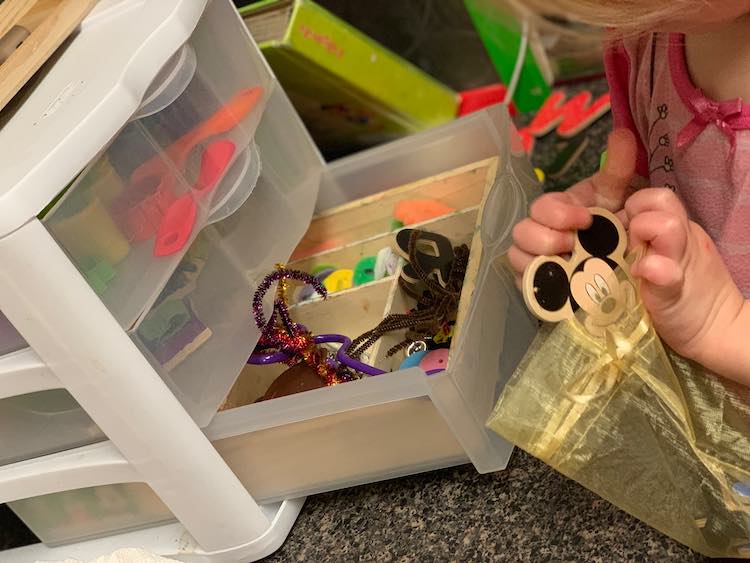 Side view from before with Zoey now putting a Mickey magnet in the bag. Behind it you can see a book of puzzles and a chalkboard between the drawers and the wall.