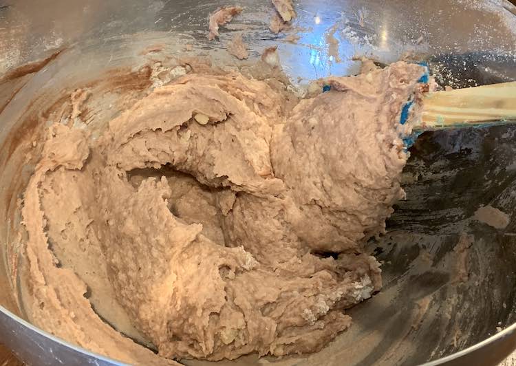 View of a metal bowl with brown sludge in it. You can see a mostly covered blue spatula in the bowl, used for mixing, and streaks of dark brown, unmixed, paint along the side.