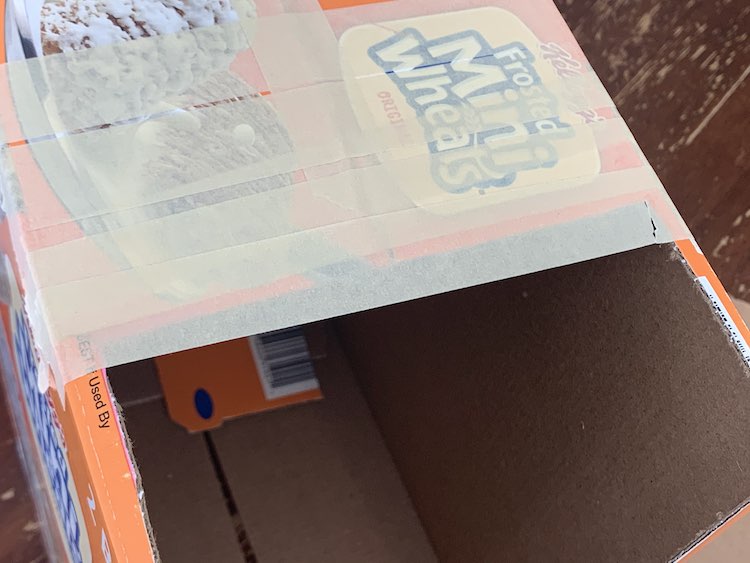 View of the top of the box showing the last piece of tape stretching across the width of the box overlapping with the cut edge. The right side has a rip in the tape leading to that corner.