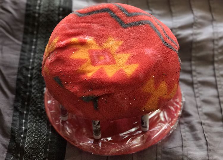 Upside down view of the felt pen holder showing the soft flannel bottom of the holder. Then pens in the holder are keeping the base upright above the plastic wrapped red plate.