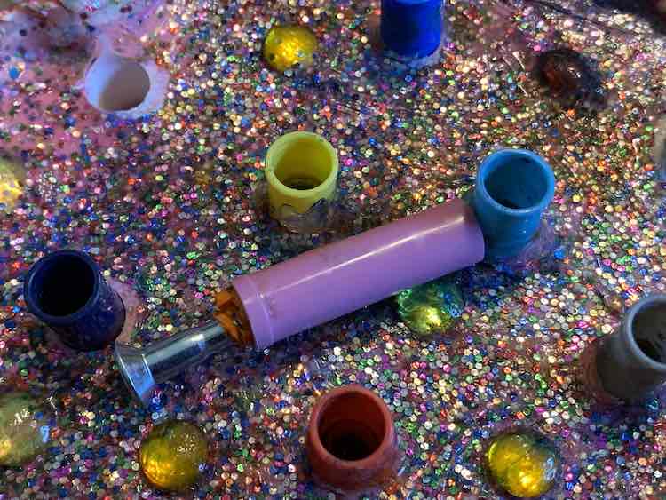 Closeup of the top of the felt pen holder showing the open lids and one open hole in the plaster. Among the lids lays a single lid on it's side with a bit of orange crayon sticking out and a metal screw.