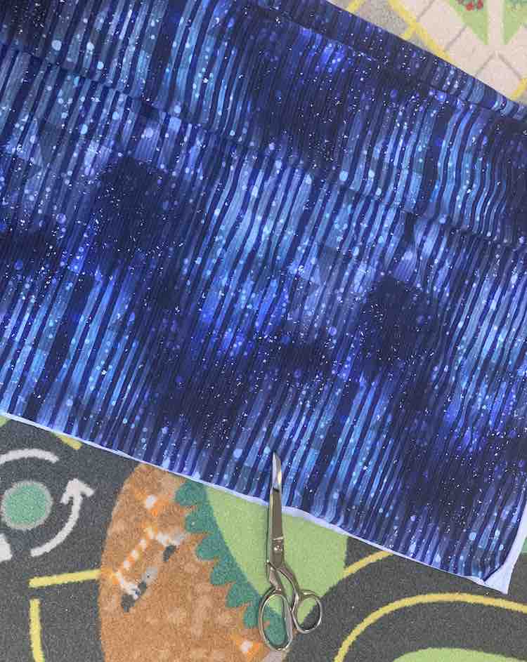 The fabric is shown folded in half and laying on top of the car mat in our living room. The bottom is cut with scissors laying overtop and