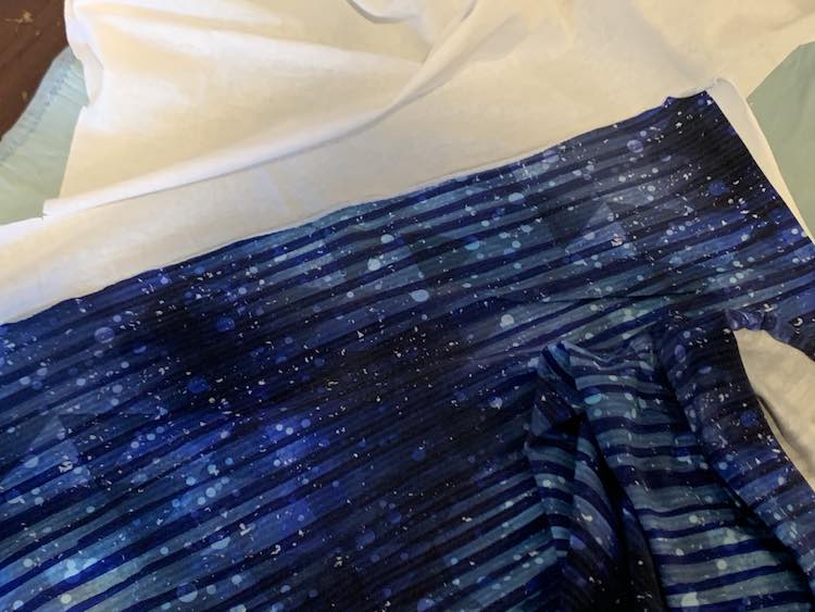 Closeup of the edge of the blue striped cotton spandex fabric laid out over the white interfacing.
