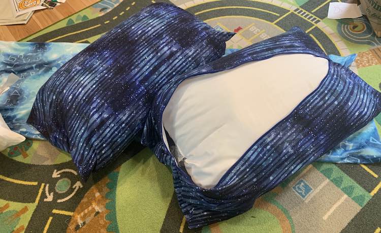 Closeup view of the matching blue striped pillows with a standard pillow inside them. The one on the left is zipped with the zipper hidden underneath it. The pillow on the right is zipper side up unzipped so you can see how much space is at the end. It's laying on the long custom Stargate pillow, will be shown in the next section, and is on the car mat.