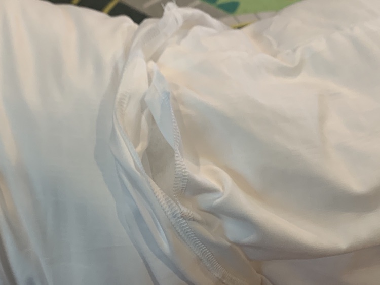 Closeup of the two pillows joined with the edges mostly overlapping. The center top of it is pulled apart so you can see both edges and the stuffing in the middle.