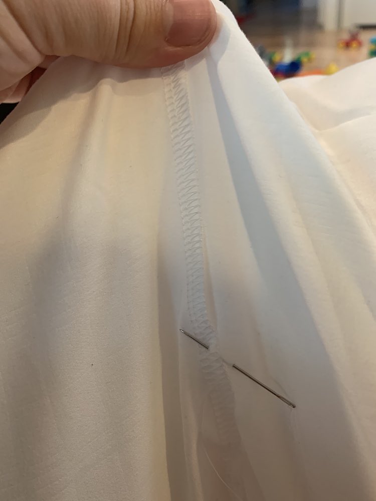 Closeup of the serged edge as I hold the one part of the join up so the fabric underneath is pulled taunt. The needle is sitting through the layers of fabric while I take the picture with my other hand. In the background, to the right, you can see part of the pillow and DUPLO, blurred out, on the floor.