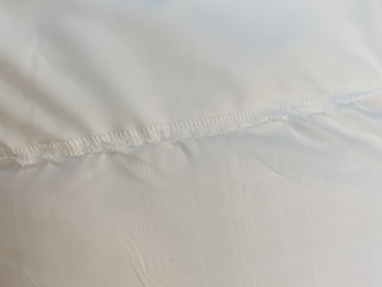 Closeup of the overlapped hand sewn seam. You can see the finished serge end of the one pillow. The seam puckers and ripples from the hand stitching that's hard to differentiate from the serged edge.