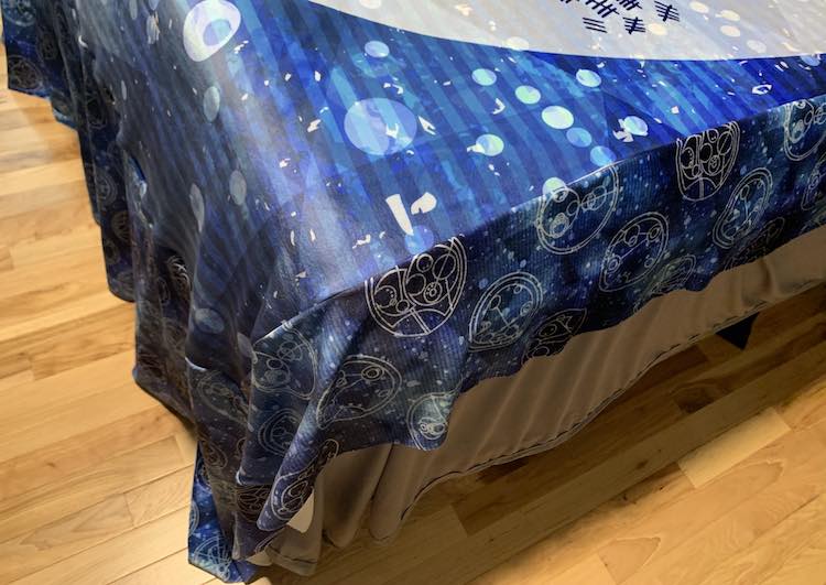 Closeup view of the corner of the bed showing the blanket just hitting the floor at the foot of the bed and laying much higher on the side allowing the sheet to dangle lower.