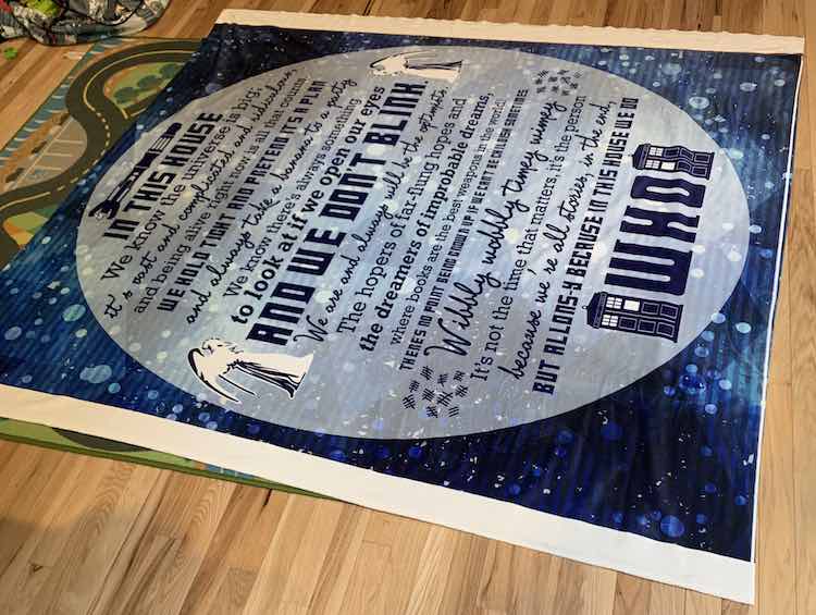 The blanket topper is laid out in the living room with our cars mat showing under the left side. Around it is hardwood and in the top left our Duplo bag.