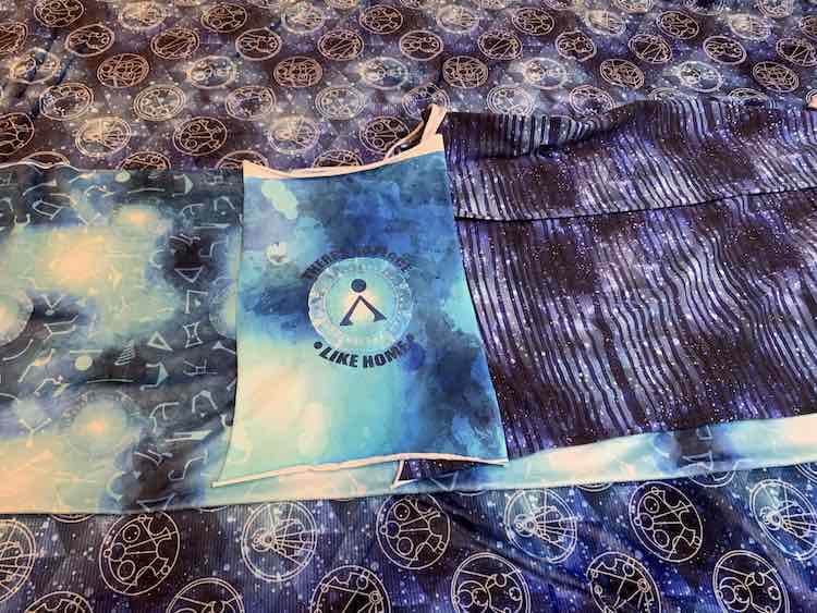 Most of the fabric laid out in one photo. The blanket topper is missing in this picture but the rest are showing. The background is the double plush Gallifreyan coordinate while the mink portals fabric lays across the center of the image. In the center of that lays the Stargate home cotton spandex panel with the striped cotton spandex beside it.