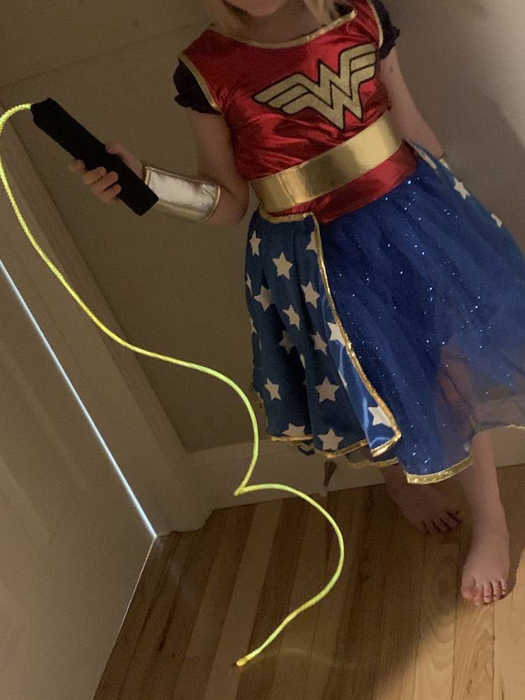 Wonder Woman holding up her lasso of truth. The black handle is in her hand and the glowing lasso hangs and drapes onto the floor.